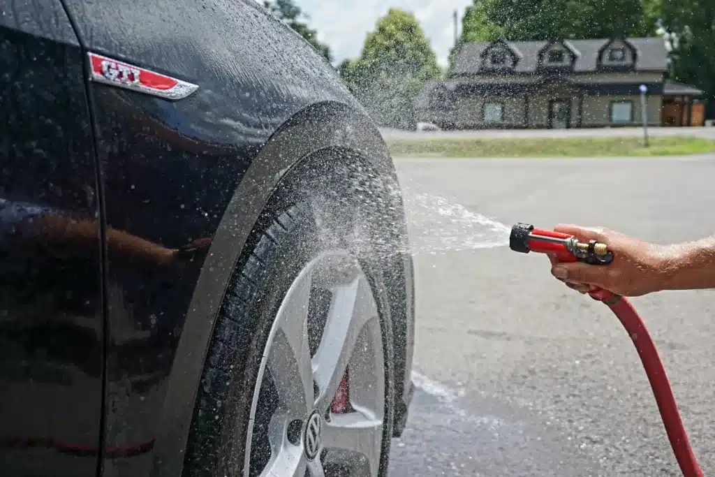 A Volkswagen GTI being washed down by a garden hose in the street
